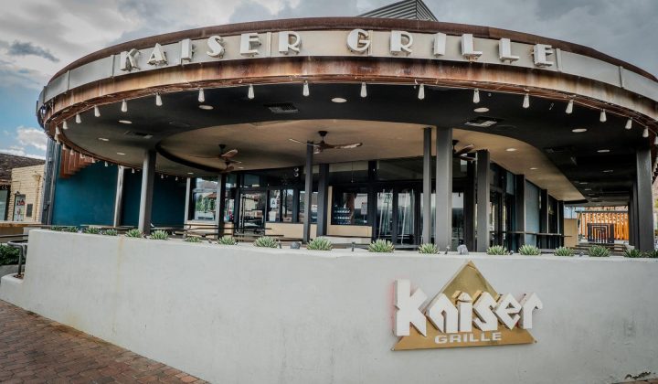 Exterior view of Kaiser Grille restaurant, featuring a curved facade, large windows, and decorative plants on a ledge.