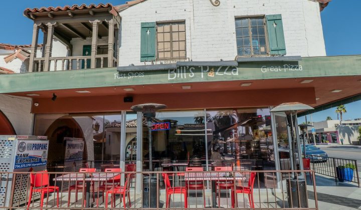 Street view of Bill's Pizza in a two-story building with outdoor seating, red chairs, and a large front window. A neon "Open" sign is visible.