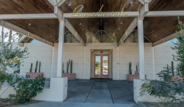 Entrance to a building with "Boozehounds" sign above. The architecture features a peaked roof and flanking cactus plants.