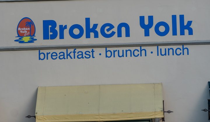 Sign for "Broken Yolk" restaurant advertising breakfast, brunch, and lunch. Logo features a yolk with a palm tree.