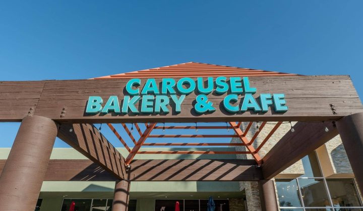 Entrance of Carousel Bakery & Cafe with blue and orange signage against a clear sky.