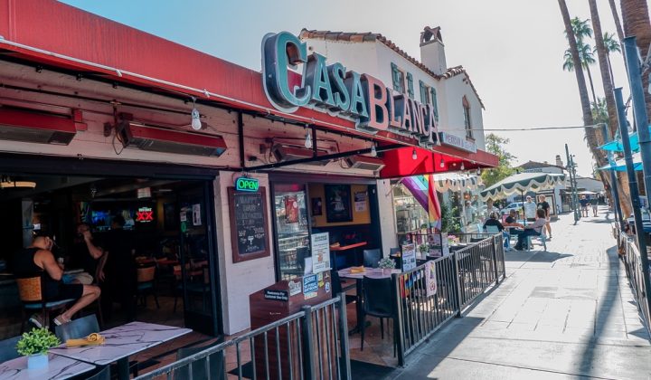Outdoor view of Casa Blanca restaurant with a red awning, open interior, people dining, and a busy sidewalk in a sunny street setting.