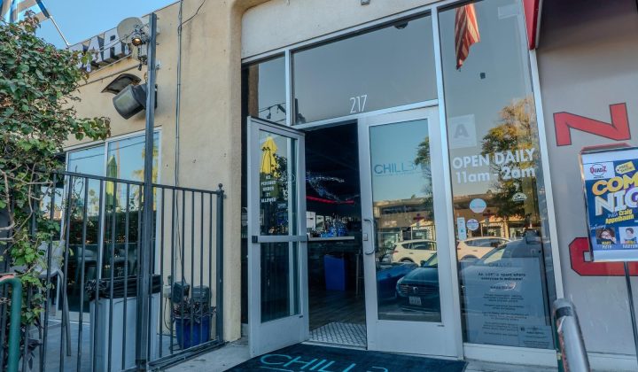 Entrance of Chill Bar with glass doors open. Signs advertise "Open Daily 11am-2am" and "Comedy Night." A mat with the bar's name is on the ground.