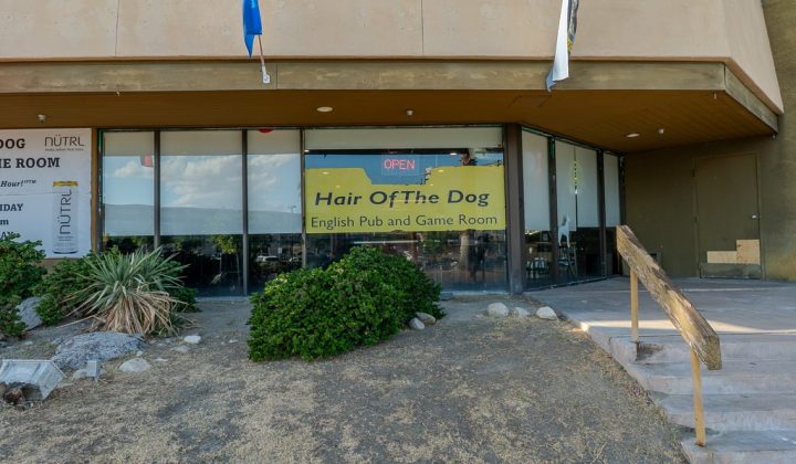 Exterior of "Hair Of The Dog" English Pub and Game Room with a yellow sign and glass windows. An open sign is visible above the entrance.