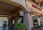 Entrance of "Happy Sushi" restaurant with a sign above the door, glass doors, and outdoor seating.