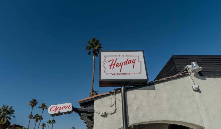 Signs for "The Heyday" and "Open" against a clear blue sky, with palm trees in the background.
