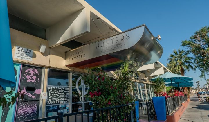Outdoor view of Hunters Nightclub with a sign reading "Spirits Elevated." The entrance is adorned with plants and shaded seating under blue umbrellas. A mural decorates the side wall.