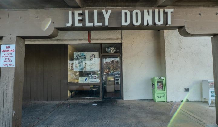 Entrance of a donut shop named "Jelly Donut" with a "Closed" sign on the door, surrounded by various vending machines and a "No Smoking" sign nearby.