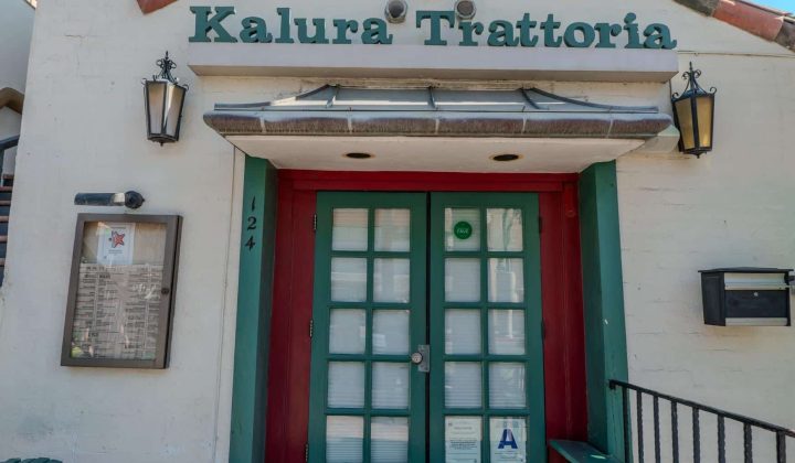 Front entrance of Kalura Trattoria with green-framed glass doors, a menu display, and an 'A' grade sign.