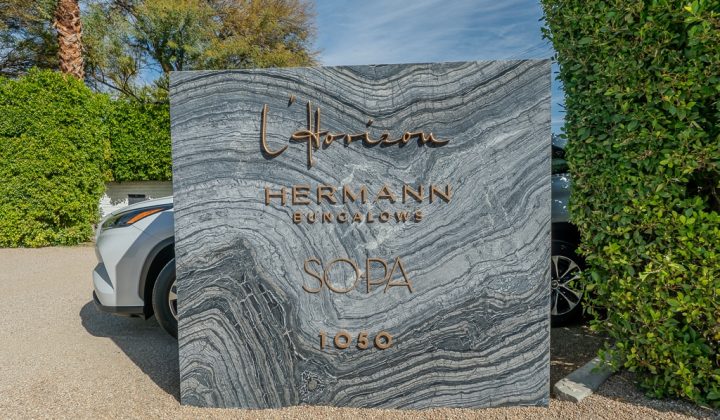 Stone sign with cursive text "Horizon," "HERMANN Bungalows," "SOPA," and "1050," positioned between green hedges and cars.