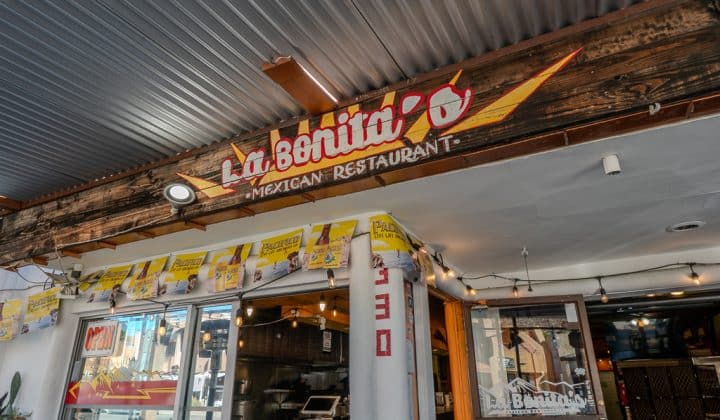 Entrance of La Bonita's Mexican Restaurant, featuring a wooden sign with yellow and red lettering, a glass door, and string lights above.
