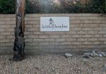 Sign on brick wall reads "Little Paradise Hotel" with palm tree logos; gravel and a tree in front.