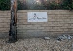 Sign on a brick wall reads "Little Paradise Hotel" above gravel and next to a tree, with foliage in the background.