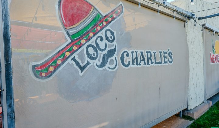 Sign on a wall with a painted sombrero and the words "Loco Charlies" in stylized letters.