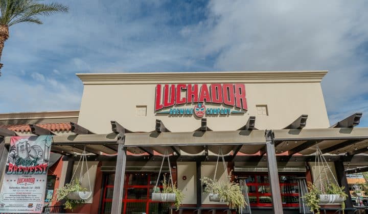 Entrance of Luchador Brewing Company with hanging plants and a sign about an event called "Beer + Breakfast" on March 12 and 13.