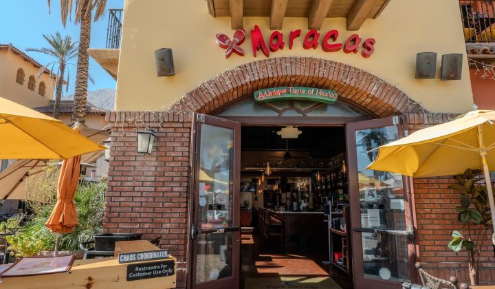 Exterior of Maracas restaurant with open double doors. Signs read "America's Taste of Mexico" and "CHAOS COORDINATOR." Yellow umbrellas and plants are visible outside.