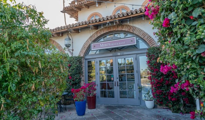 Entrance to Miro's Restaurant with arched windows, surrounded by vibrant bougainvillea plants and outdoor seating.