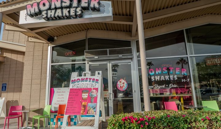 Storefront of "Monster Shakes" with colorful chairs outside and a menu board displaying milkshake options. The sign indicates the shop is open.