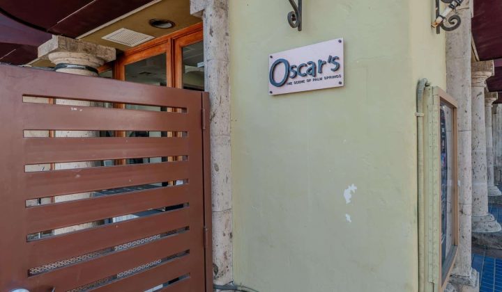 Gate leading to a building with a sign that reads "Oscar's Fine Foods and Beverages" attached to a beige wall.