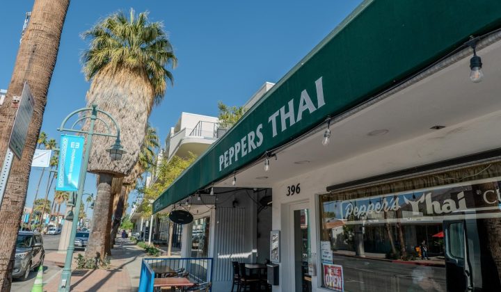 Street view of Peppers Thai restaurant with a green awning in a sunny area, palm trees nearby, and a "Yes, we're open" sign in the window.