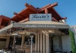 Exterior of Riccio's restaurant with signage for steak, seafood, and pasta under a red angular roof. White fairy lights hang from the awning.