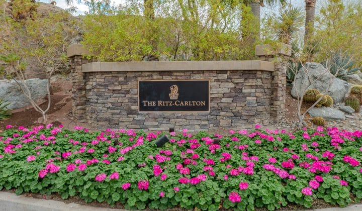 Stone sign with "The Ritz-Carlton" logo, surrounded by pink flowers and greenery.