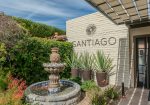 Garden area with a stone fountain and potted plants next to a building wall with "Santiago" written on it.
