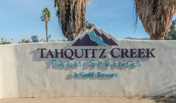 Sign for Tahquitz Creek Palm Springs Golf Resort, featuring mountain design and surrounded by palm trees.