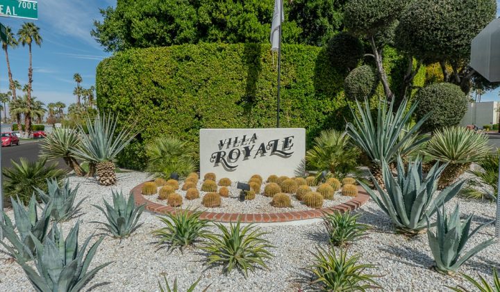 Entrance sign for Villa Royale surrounded by desert plants, including agave and cacti, under a clear blue sky.