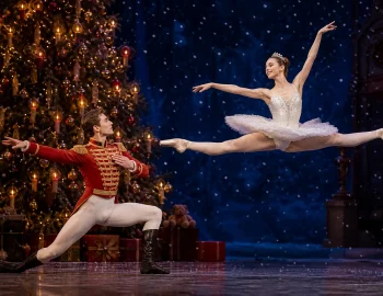 Nutcracker prince and ballerina on stage with a lit Christmas tree