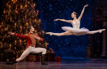 Nutcracker prince and ballerina on stage with a lit Christmas tree
