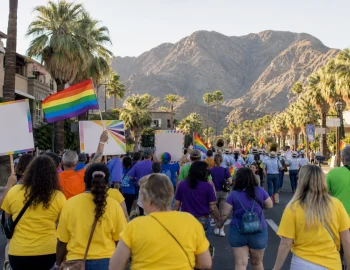 Walkers with rainbow flags on a palm-lined desert street